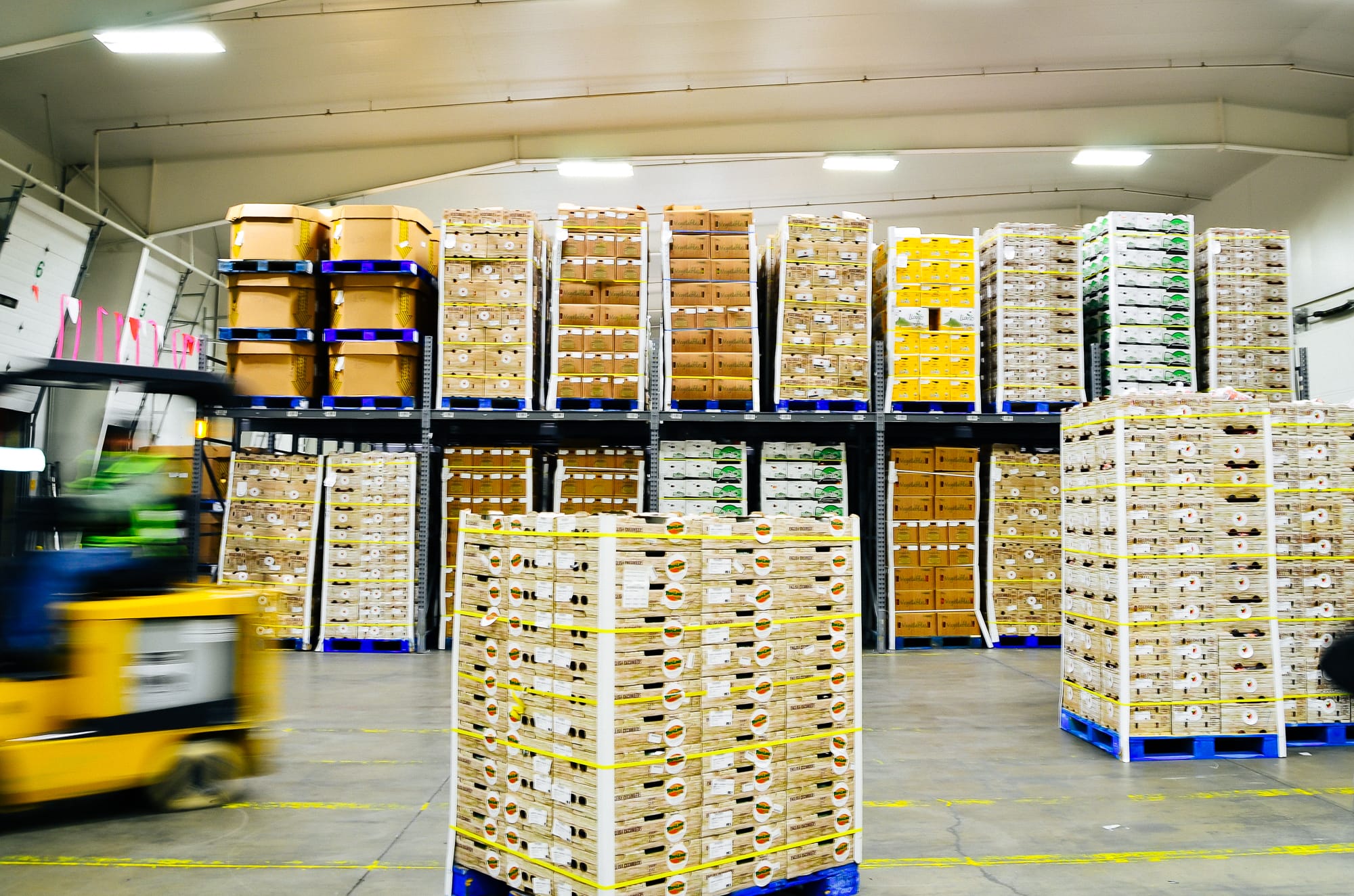 Produce warehouse floor with pallet racks of packed cases and a forklift in the aisle